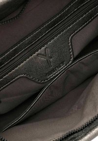 Interno di una borsa in pelle nera con due scomparti con zip, caratterizzato da una texture liscia e un sottile logo impresso su una patch nera.