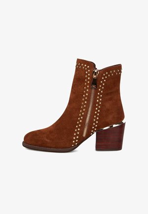 Bruine suède enkellaarzen met gouden studs, een zijrits en een gestapeld houten hak. Gladde textuur, taps toelopende vorm en een elegant ontwerp.
