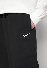 Černé tepláky vyrobené z bavlněné směsi s bílým logem Nike. Mezi vlastnosti patří boční kapsy a elastický pas pro pohodlí.
