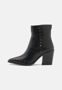 Bota de cuero negra hasta el tobillo con punta afilada, detalles texturizados en la parte delantera y tachuelas decorativas de cobre a lo largo del costado. Tacón cuadrado.