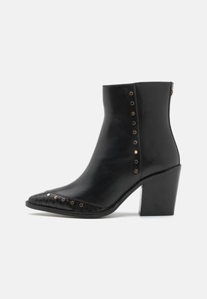 Bottine en cuir noir avec un bout pointu, des détails texturés à l'avant et des clous décoratifs en cuivre sur le côté. Talon carré.