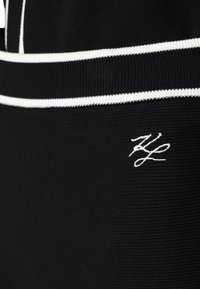 Black fabric with a ribbed texture, featuring white horizontal stripes and a white embroidered logo at the lower left corner.