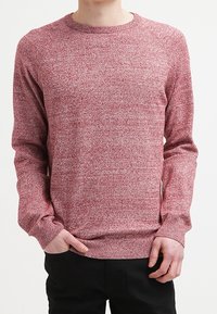 Röd texturerad tröja med rund halsringning och långa ärmar. Den har ett subtilt melerat mönster och ribbade muddar och nederkant.