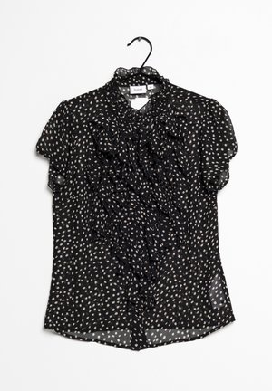 Zwarte semi-transparante blouse met crèmewitte stippen, geruffleerd voorpand, korte mouwen en een hoge kraag. Licht, soepel vallend stof.