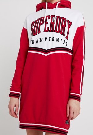 Czerwona i biała długa sukienka z kapturem i długimi rękawami z tekstem "SUPERDRY CHAMPION '72" oraz paskowanymi mankietami, dołem i detalami na rękawach.