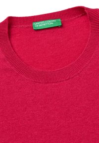 Fuchsiový svetr s kulatým výstřihem, pletenou strukturou a žebrovanými manžetami. Na výstřihu se nachází zelená visačka "United Colors of Benetton".