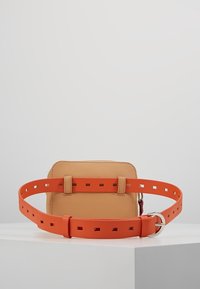 Rå läder bälteväska med rektangulär form och ett orange justerbart bälte med fyrkantiga utskärningar. Silverfärgad detalj synlig på spännet.