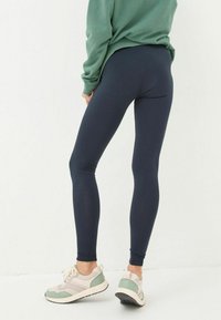 Navy leggings with a smooth texture, fitted shape, and high waist, paired with light-colored athletic shoes featuring green accents.