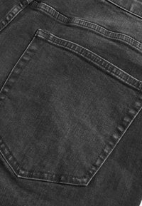 Czarny dżins z tylną kieszenią z widocznym przeszyciem i lekko wyblakłą fakturą. Prosty design bez ozdób.