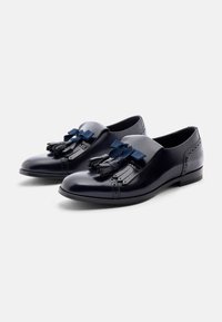 Zapatos de cuero azul marino con punta redondeada, que presentan un acabado suave, borlas decorativas y un sutil detalle de brogue en los laterales.