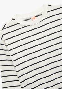 Biała bluzka z długim rękawem w czarne poziome paski, z ribbowanym okrągłym dekoltem i miękką fakturą. Prosty design, casualowy styl.