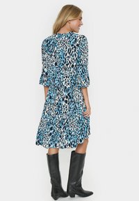 Mėlyna ir juoda leopardų rašto suknelė su sluoksniuotu dizainu ir trijų ketvirčių rankovėmis. Nešiojama su juodais iki kelių batais.