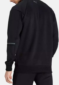 Sudadera negra con cuello alto, mangas largas y un dobladillo texturizado. Acento reflectante en la manga izquierda. Logo de la marca en la parte posterior del cuello.