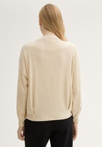 Jasno beżowy sweter z dzianiny o luźnym kroju, z opuszczonymi ramionami i długimi rękawami. Posiada okrągły dół i subtelną teksturę na całej powierzchni.