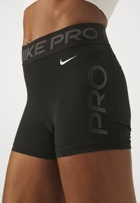 Czarne sportowe szorty z wysokim pasem, na którym znajduje się napis "PRO" w szarych literach. Wykonane z elastycznego materiału, mają smukły design.