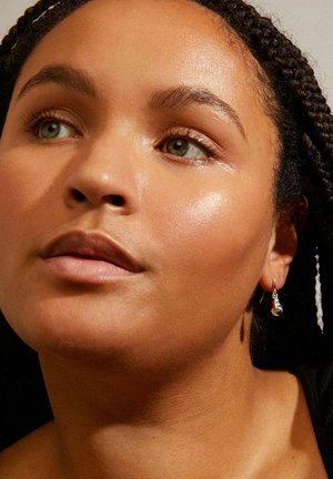 Silver drop earrings hang from a braided hairstyle. The skin has a smooth, glossy texture, with natural makeup highlighting features.