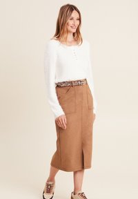 Maglione bianco soffice con scollo rotondo e dettagli in bottone, abbinato a una gonna midi in suede color tan e una cintura con stampa leopardata, completato da sneakers beige.