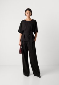 Černý dvoudílný outfit skládající se z volného topu s páskem a širokými kalhotami. Doplněný malou bordó kabelkou.