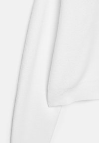 Biely flísový sveter s jemnou textúrou, s rebrovaným lemom a manžetami, strihaný v uvoľnenom tvare.