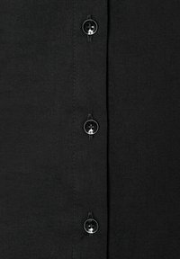 Camicia nera con chiusura frontale a bottoni neri, trama sottile e cuciture dritte lungo le giunture.