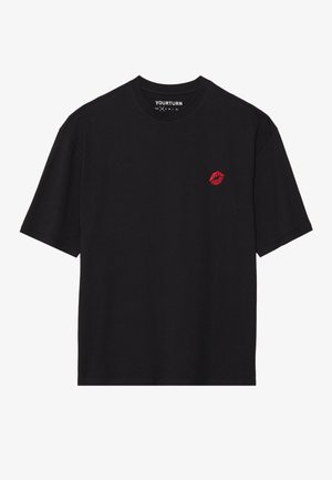 Schwarzes T-Shirt mit kurzen Ärmeln, kleinem roten Lippenmotiv auf der linken Brust und "YOURTURN"-Etikett innen im Kragen.