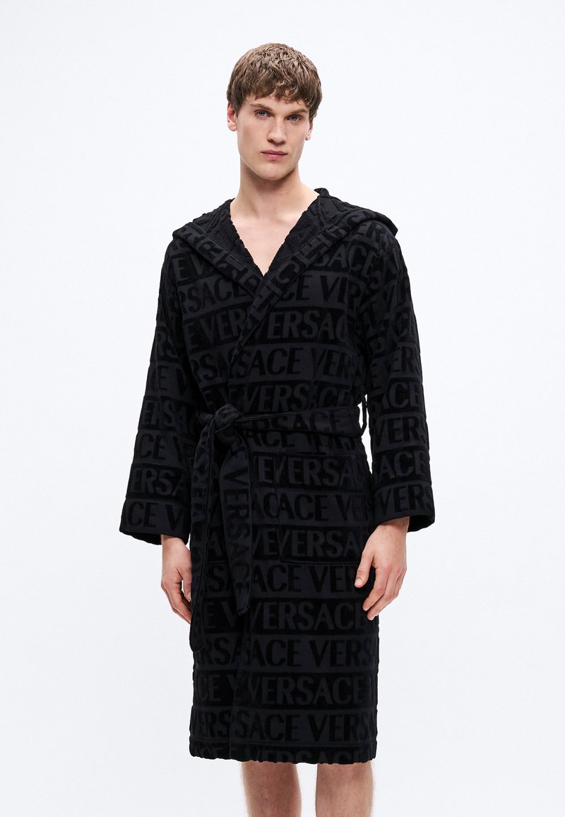 Čierny župan so štruktúrovanou tkaninou, zdobený opakujúcim sa logom "VERSACE". Má kapucňu, dlhé rukávy a opasok na previazaní v páse.