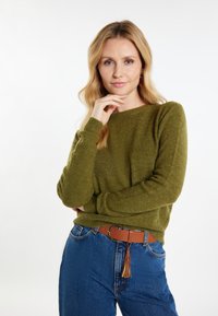Maglione verde oliva con scollo rotondo e maniche lunghe, abbinato a jeans blu a vita alta e una cintura marrone con dettaglio a frange.