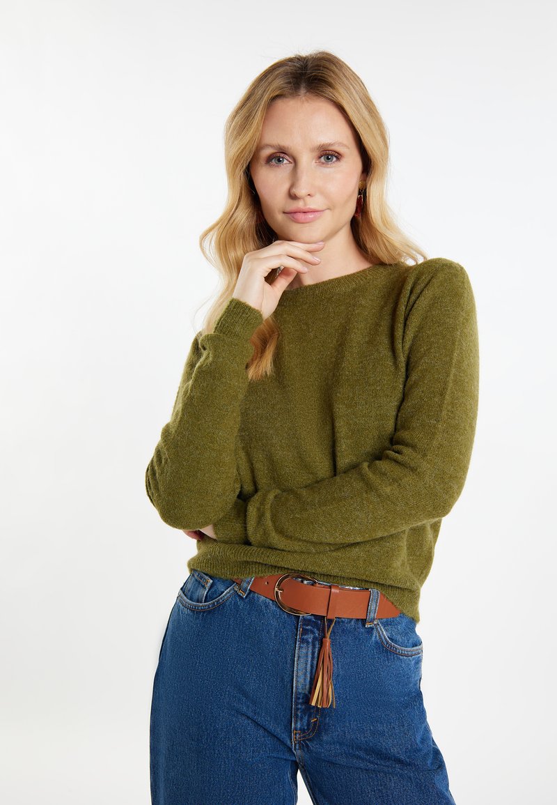 Maglione verde oliva con scollo rotondo e maniche lunghe, abbinato a jeans blu a vita alta e una cintura marrone con dettaglio a frange.