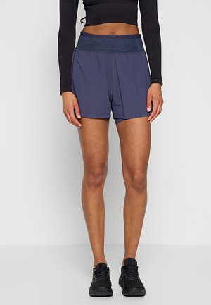Krótka, sportowa szorty w ciemnoniebieskim kolorze, z teksturowanym wzorem, szerokim pasem i lekkim materiałem. Noszone z czarnymi butami sportowymi.