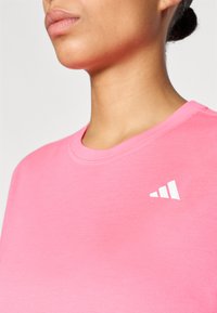 Ροζ βαμβακερό T-shirt με στρογγυλή λαιμόκοψη. Διαθέτει λευκό λογότυπο με τρεις ρίγες στην αριστερή πλευρά του στήθους. Λεί ο ύφασμα, εφαρμοστή σχεδίαση.