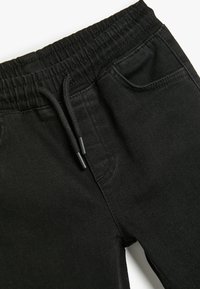 Pantalones de chándal negros hechos de una suave mezcla de algodón, con cintura elástica, cierre con cordón y bolsillos laterales. Textura suave.