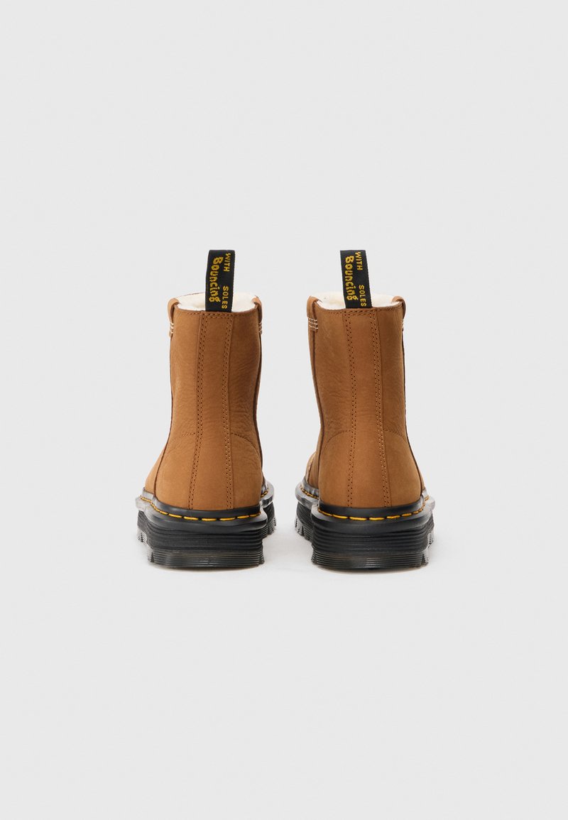Braune Leder-Ankle-Boots mit schwarzen Gummisohlen, gelben Nähten und Ziehschlaufen, die den Text "MIT BOUNCING SOLE" zeigen. Strukturierte Oberfläche.