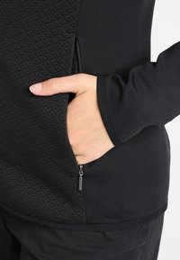 Top nero a maniche lunghe con pannello laterale testurizzato a motivo diamante e tasca con cerniera in vita, realizzato in un tessuto morbido e con design senza cuciture.