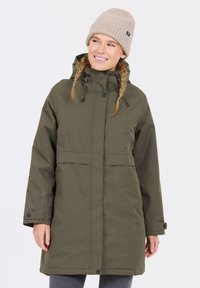 Lång olivgrön parka med dragsko-hood, tryckknappar och elastiska ärmslut. Bärs med en ljusbeige stickad mössa.