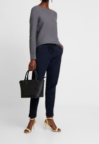 Szary sweter o fakturze, granatowe spodnie z troczkami, żółte sandały na obcasie oraz czarna torba z złotymi akcentami. Minimalistyczny design, nowoczesny styl.