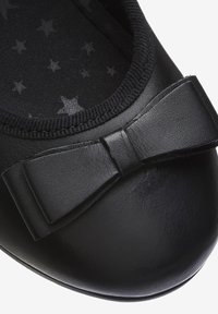 Ballet plat en cuir noir avec un bout rond et un accent en nœud. La doublure intérieure texturée présente un motif d'étoiles. Une bordure élastique entoure l'ouverture.