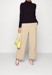 Černý rolák, béžové široké kalhoty, žlutá kabelka přes rameno a multibarevné vzorované boty. Vystupují texturované materiály.