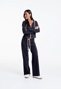 Dark navy zip-up hoodie with white drawstring, paired with wide-leg navy sweatpants. Model wears white sneakers. Simple, soft cotton fabric.