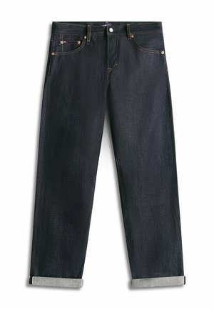 Proste ciemnoindygo dżinsy z podwiniętymi nogawkami, miedzianymi nitami i zapięciem na guziki z przodu na białym tle.