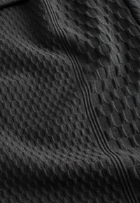 Schwarzer, strukturierter Stoff mit einem erhabenen, geometrischen Muster und vertikalen Linien. Weiches Material mit einem leichten Glanz.