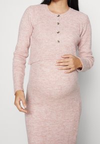 Ljusrosa ribbad stickad graviditetströja med rund hals, kort design, fyra neutrala knappar och långa ärmar.