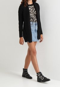 Czarny dzianinowy kardigan, bluzka w zwierzęcy wzór, jeansowa spódnica oraz czarne botki z ćwiekami i dużymi metalowymi elementami. Strój cechuje się warstwowaniem tekstur.