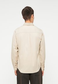 Μ�πεζ μπλούζα με μακριά μανίκια, κανονική γραμμή, κουμπιά στον καρπό και επίπεδο γιακά. Λείος υφασμάτινος σχεδιασμός, λεπτομέρεια νωτού στην πλάτη και πλαϊνές σχισμές στο στρίφωμα.