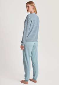 Lichtblauw gestreepte langemouwen top met ronde hals, gecombineerd met effen lichtblauwe broek met elastische boorden. Zachte, comfortabele stof.