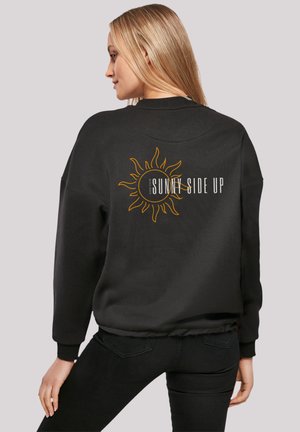 Black sweatshirt with a round sun graphic and "SUNNY SIDE UP" text. Features ribbed cuffs and waistband; soft, textured fabric.