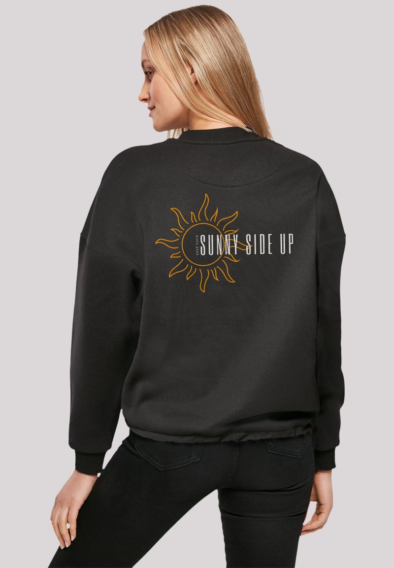Black sweatshirt with a round sun graphic and "SUNNY SIDE UP" text. Features ribbed cuffs and waistband; soft, textured fabric.