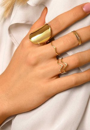 Gouden sieraden op een hand: een gladde, ronde ring, drie slanke ringen met verschillende ontwerpen - één golfvormig, één zigzag en één eenvoudige band.
