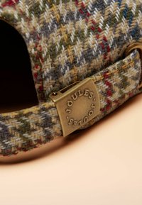 Tweedpet met een ruitmotief in groen, blauw en bruin, met een koperen zijclip waarop "Joules" is gegraveerd. Zachte textuur.