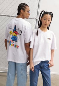 White oversized t-shirts feature colorful graphic designs: one has a coffee-themed illustration, and the other displays a small multicolored logo.