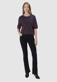 Korte mouwen, cropped paarse sweatshirt met een ronde hals, gecombineerd met zwarte uitlopende jeans en zwarte enkellaarsjes met hak. Gladde stoftextuur.